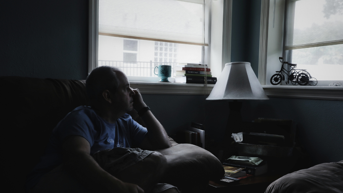 Man sitting on bed holding head, overwhelmed and exhausted from daily stress