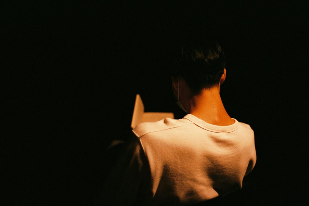 Person standing quietly in low light, representing emotional exhaustion and feeling tired despite being physically healthy.