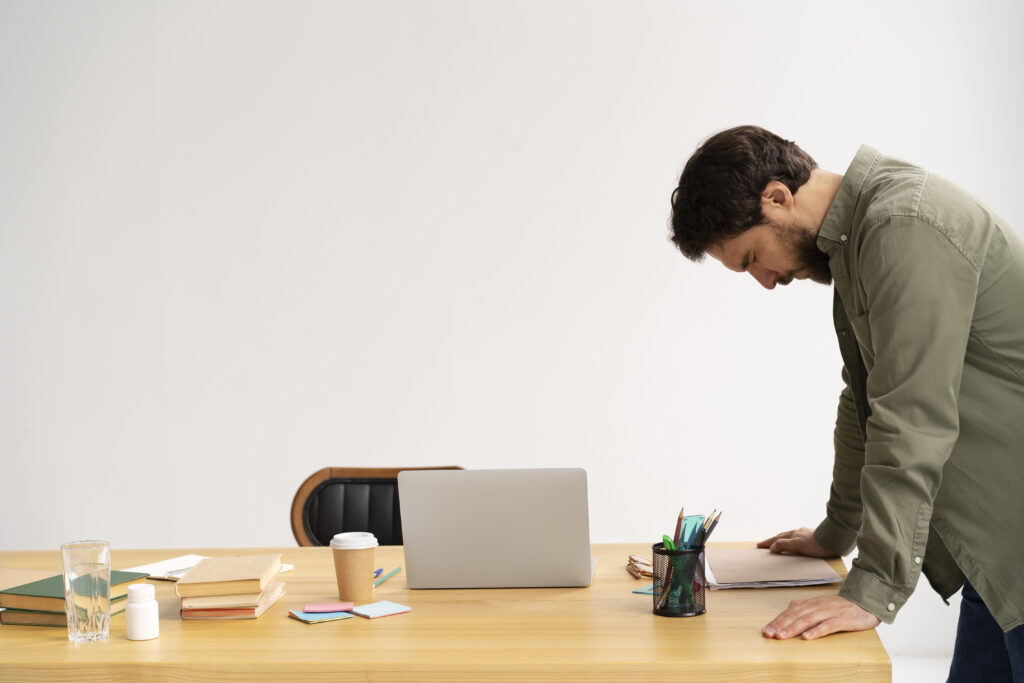 person slouched at desk midday looking drained with hand near stomach