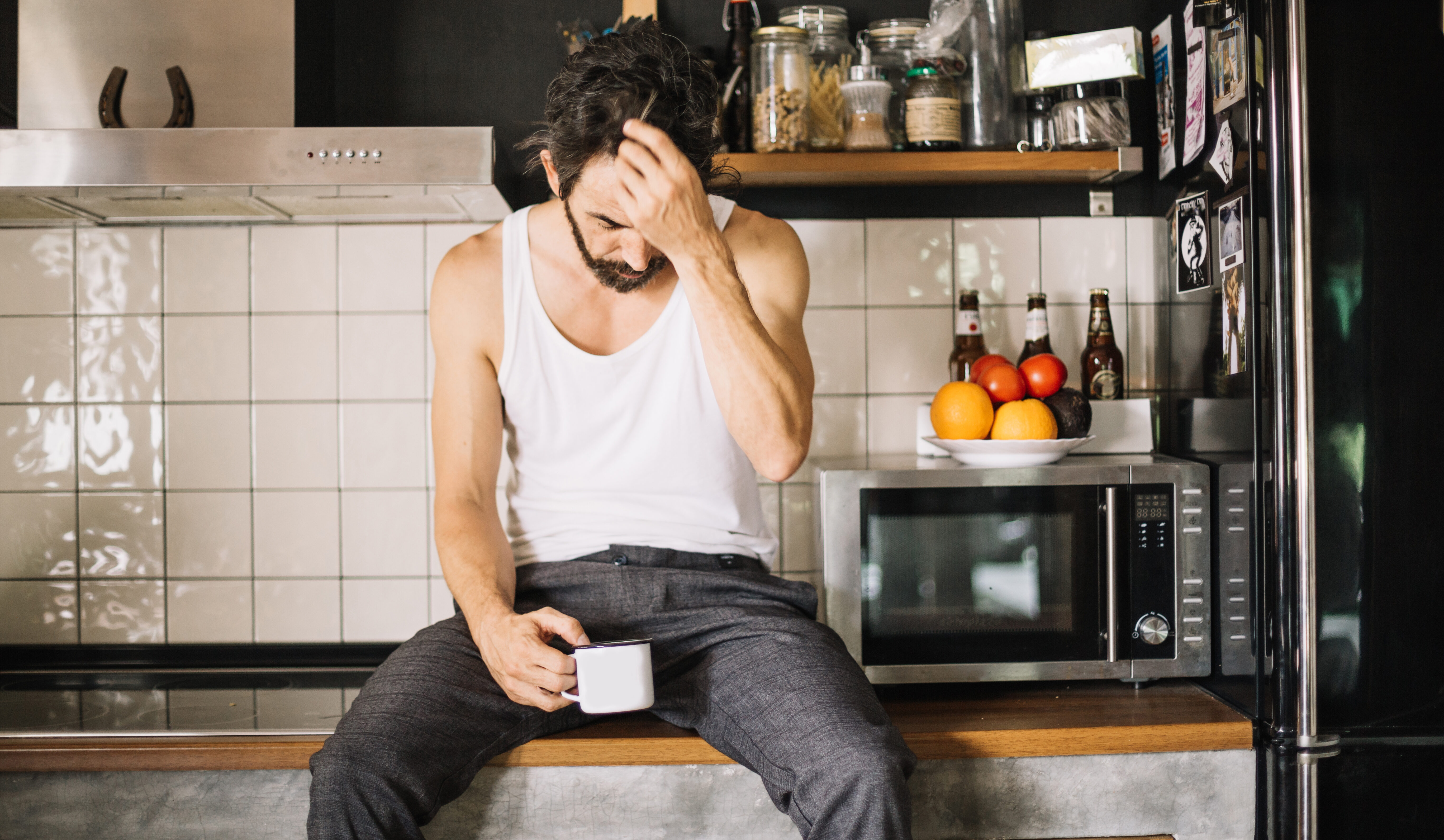 person sitting at kitchen table looking tired holding a morning coffee