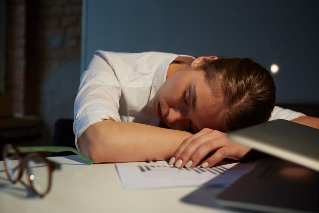 person sitting on the edge of bed in the morning with head in hands looking exhausted and unrestored